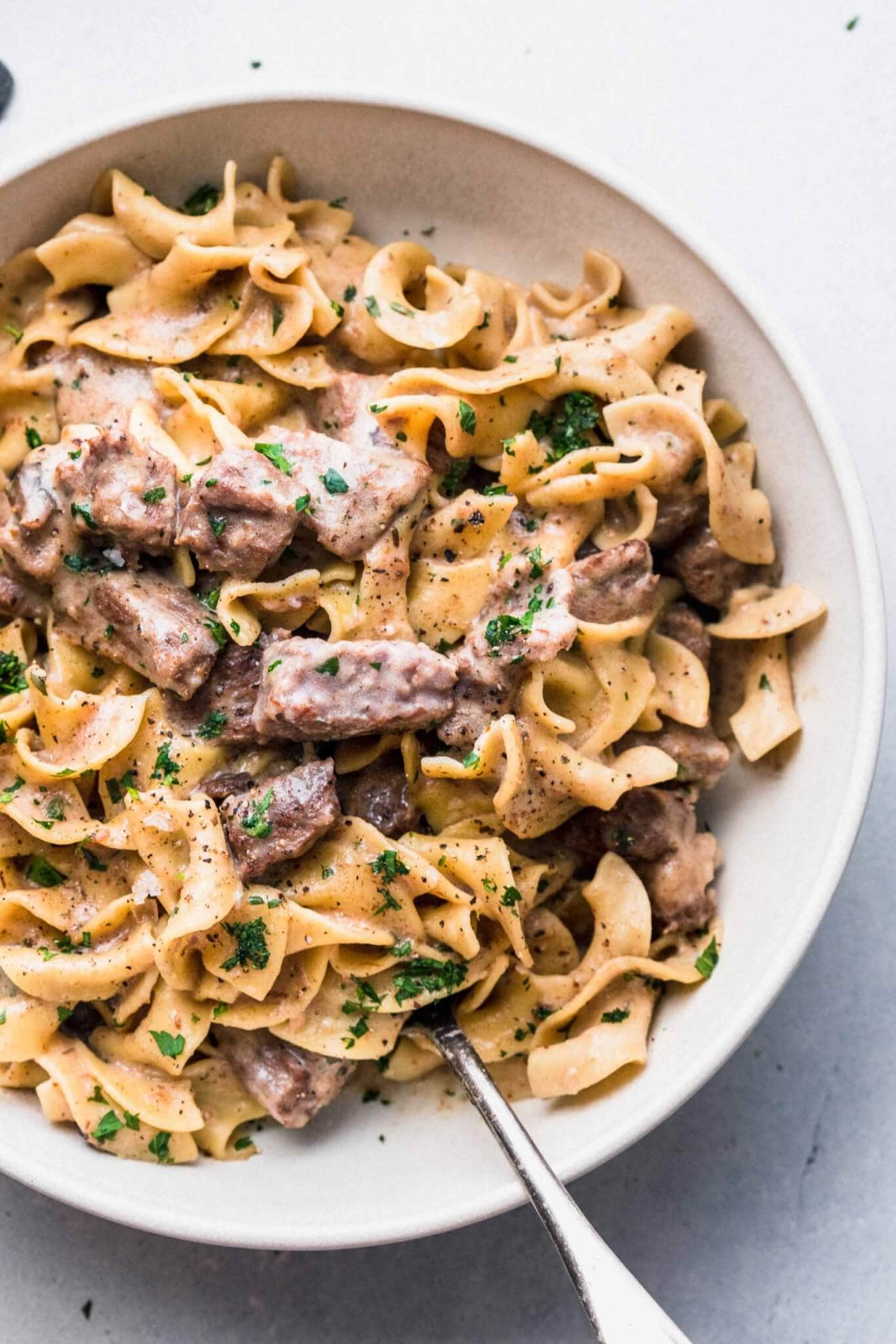 Beef stroganoff in large white bowl with serving spoon.