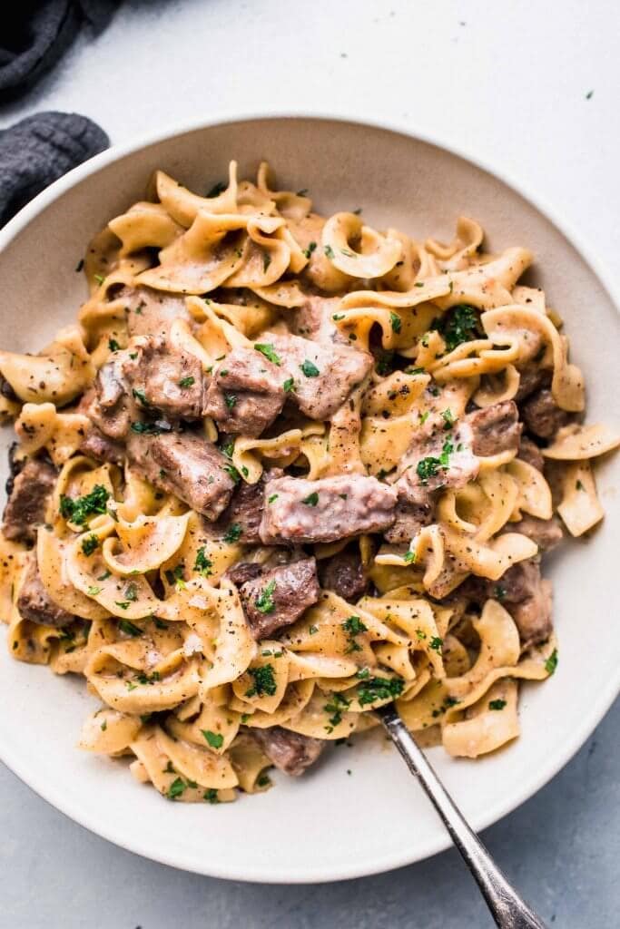 Overhead shot of beef stroganoff in large white bowl with spoon.