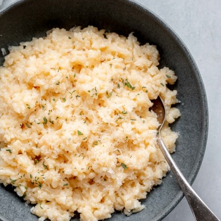 Risotto in grey bowl next to shards of parmesan cheese.