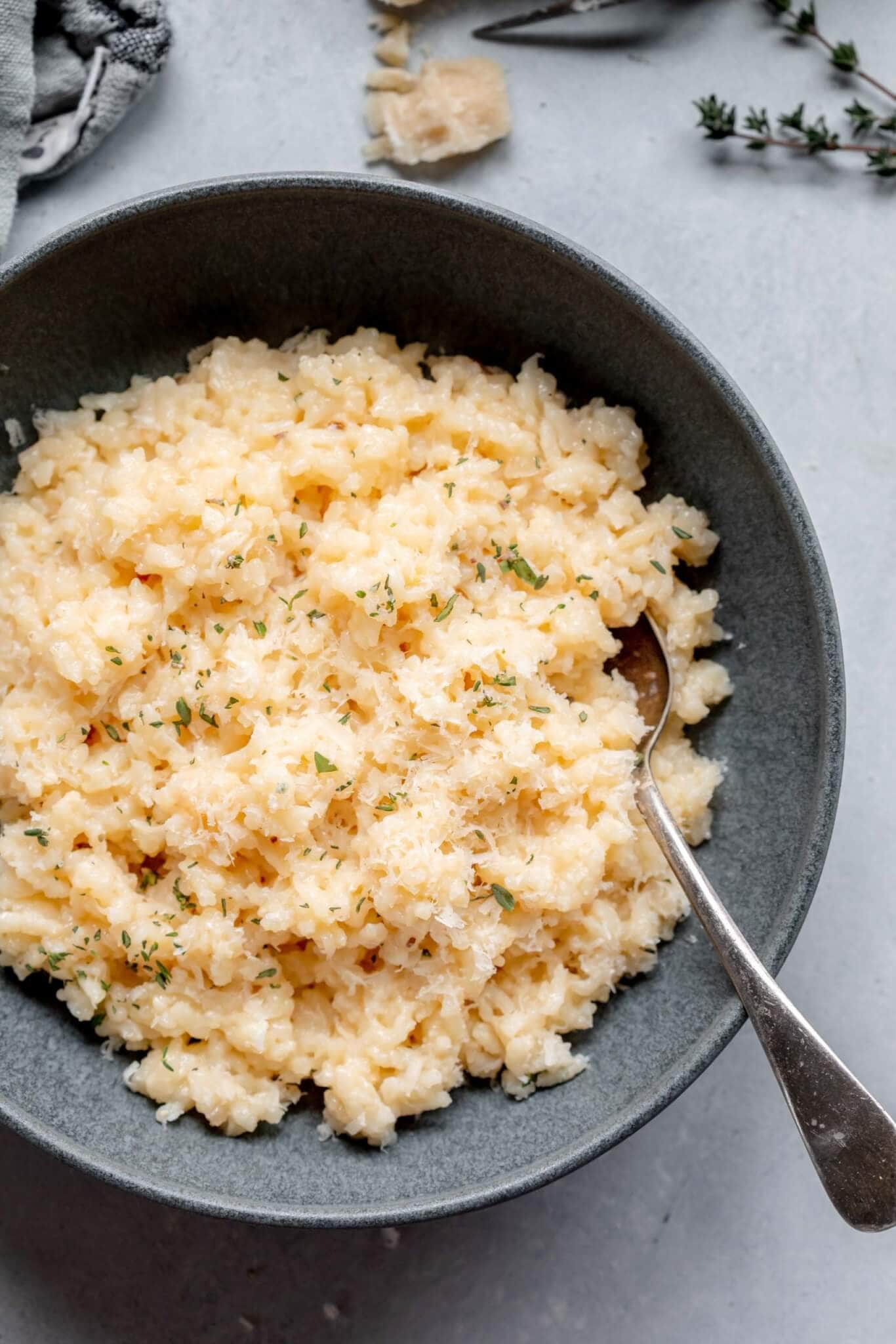 Risotto in grey bowl next to shards of parmesan cheese.