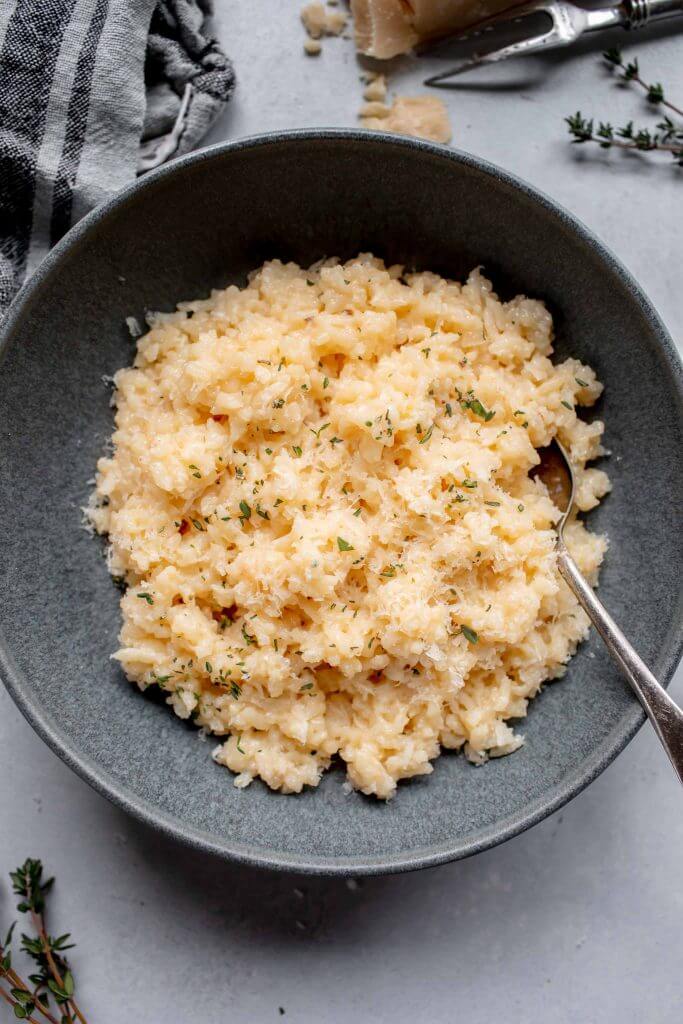 Risotto in grey bowl next to shards of parmesan cheese.