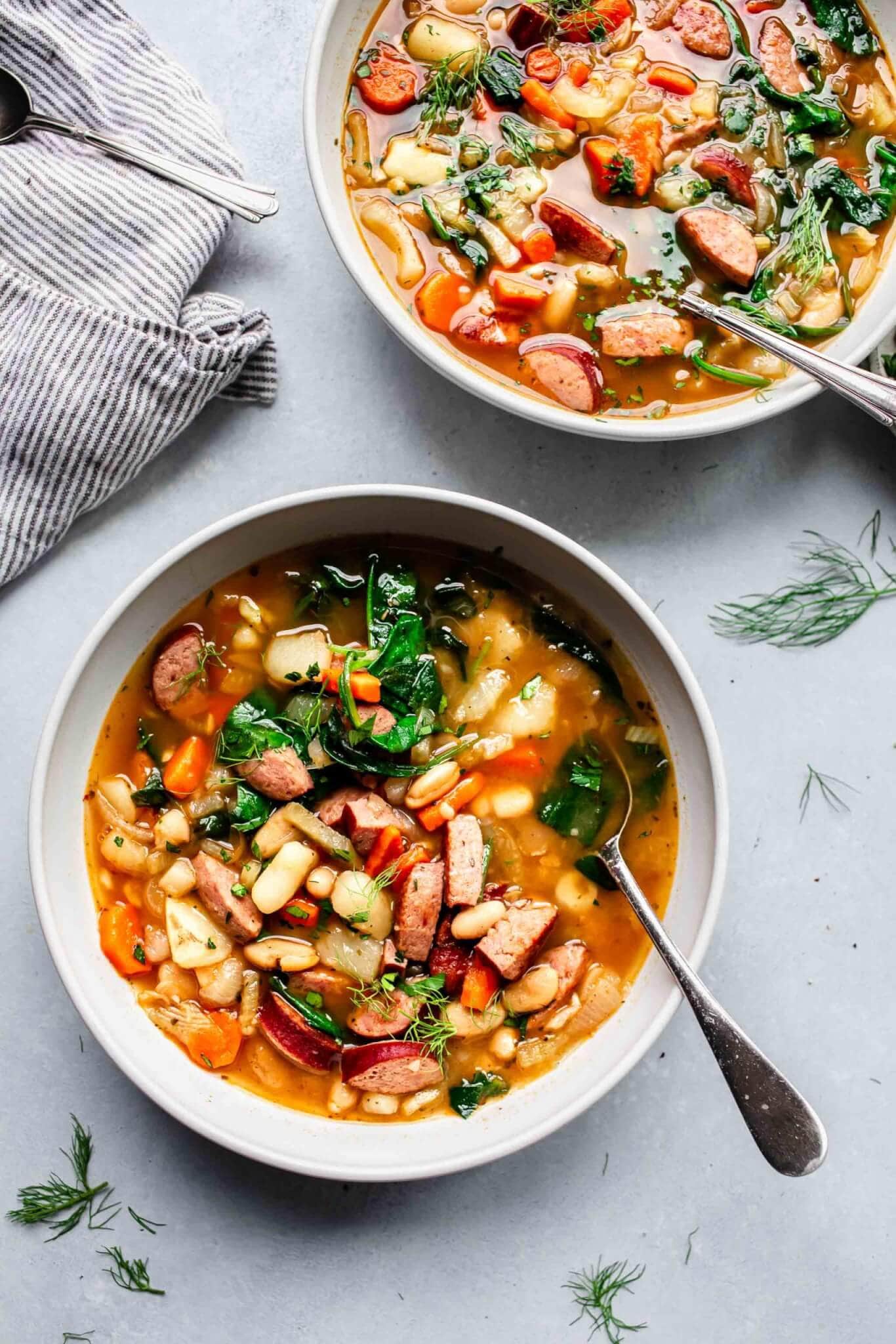 Overhead of two bowls of kielbasa soup with spoons and fresh parsley garnish