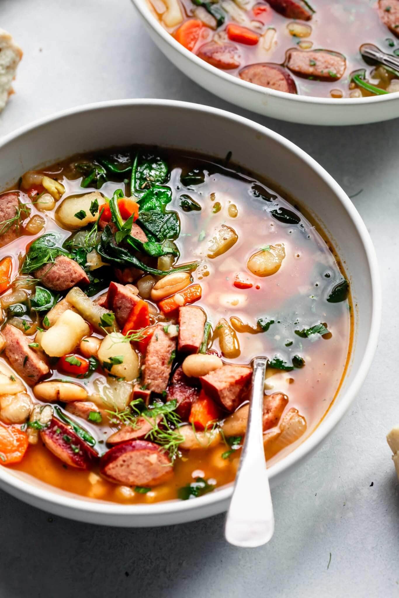 Two bowls of kielbasa soup with spoons
