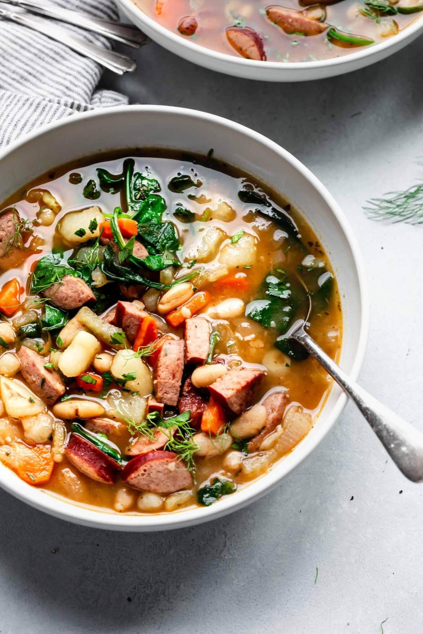 Bowl of kielbasa soup with a spoon and second bowl in background