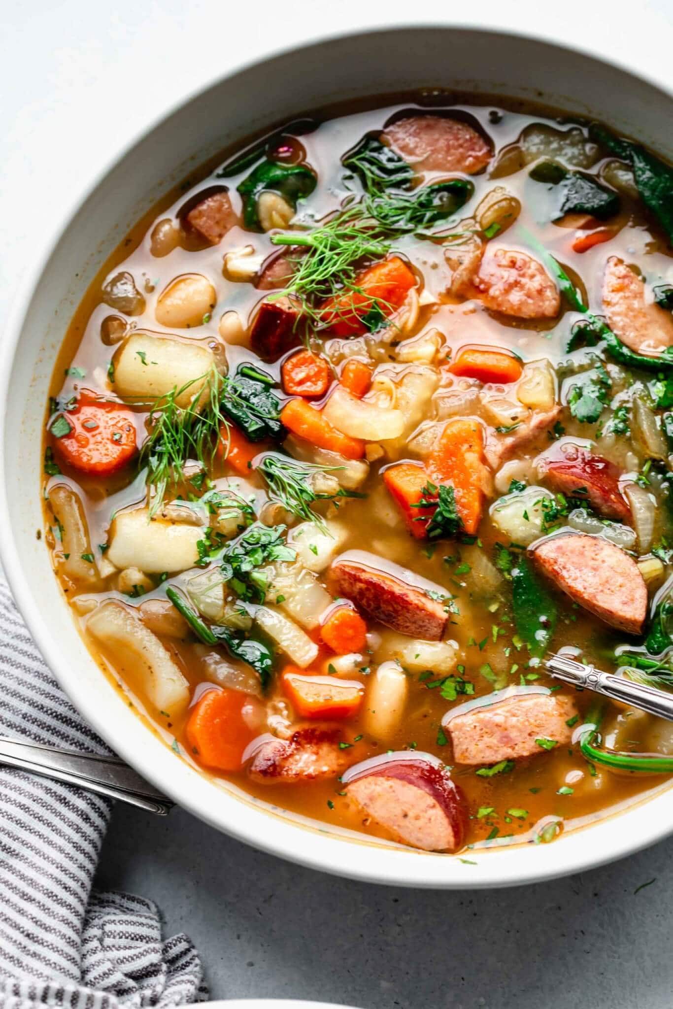 Close up bowl of Polish kielbasa soup with towel on counter