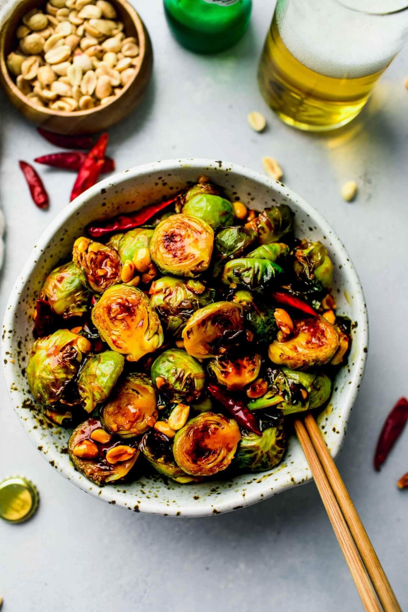Bowl of Kung Pao Brussels Sprouts on counter with bowl of peanuts and jar of oil