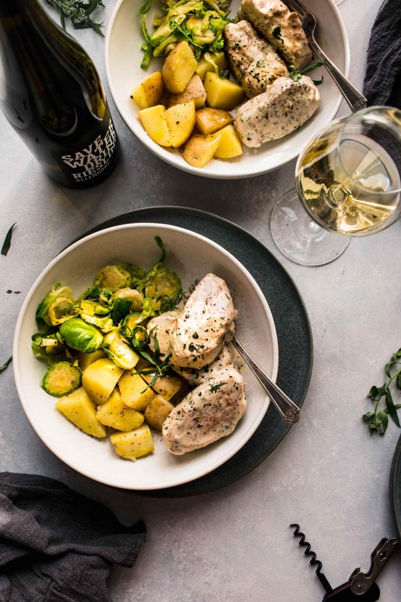 Two serving plates of pork with brussels sprouts and white wine. 