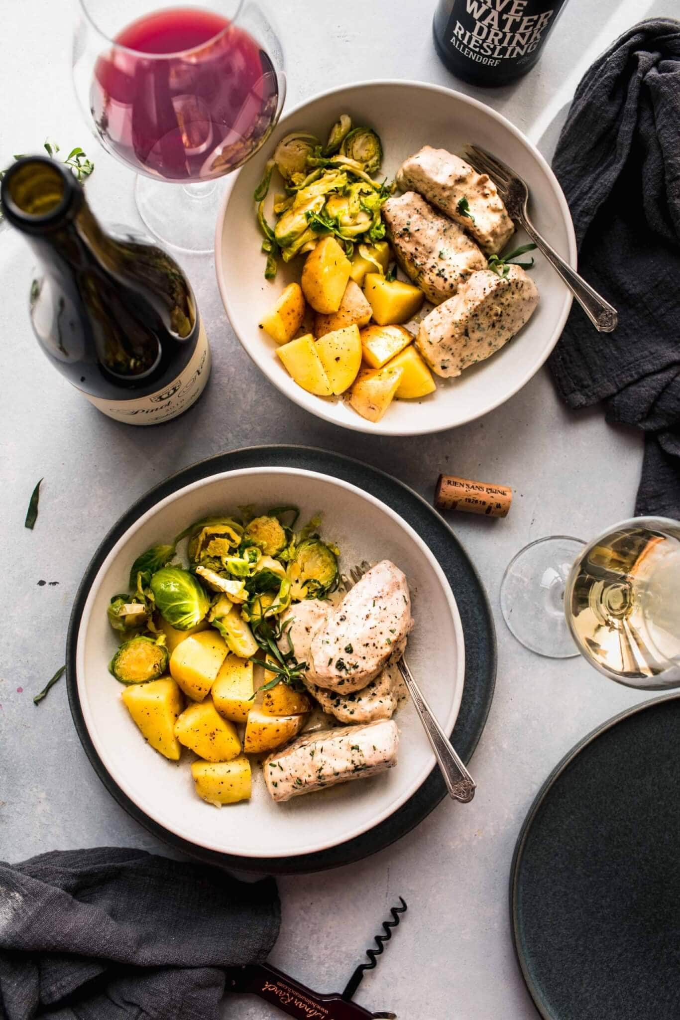 Two serving plates of pork medallions next to red wine. 