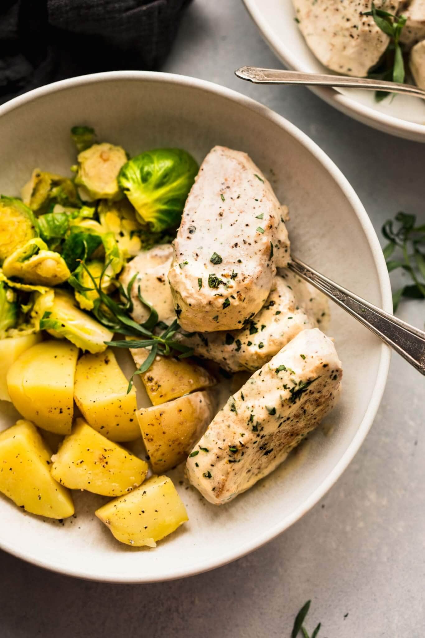 Pork medallions, potatoes, and brussels sprouts in white bowl.