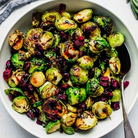 Roasted brussel sprouts in bowl drizzled with balsamic glaze and sprinkled with cranberries.