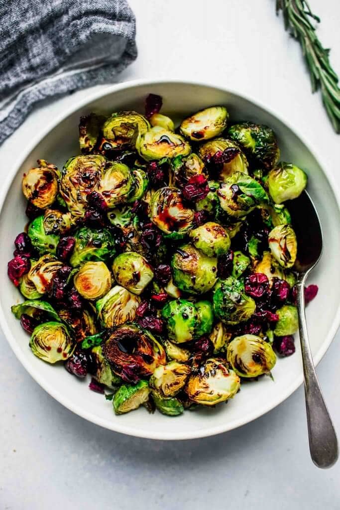 Roasted brussel sprouts in bowl drizzled with balsamic glaze and sprinkled with cranberries.