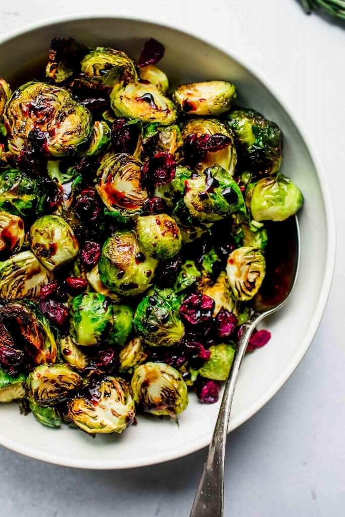 Roasted brussel sprouts in bowl drizzled with balsamic glaze and sprinkled with cranberries.