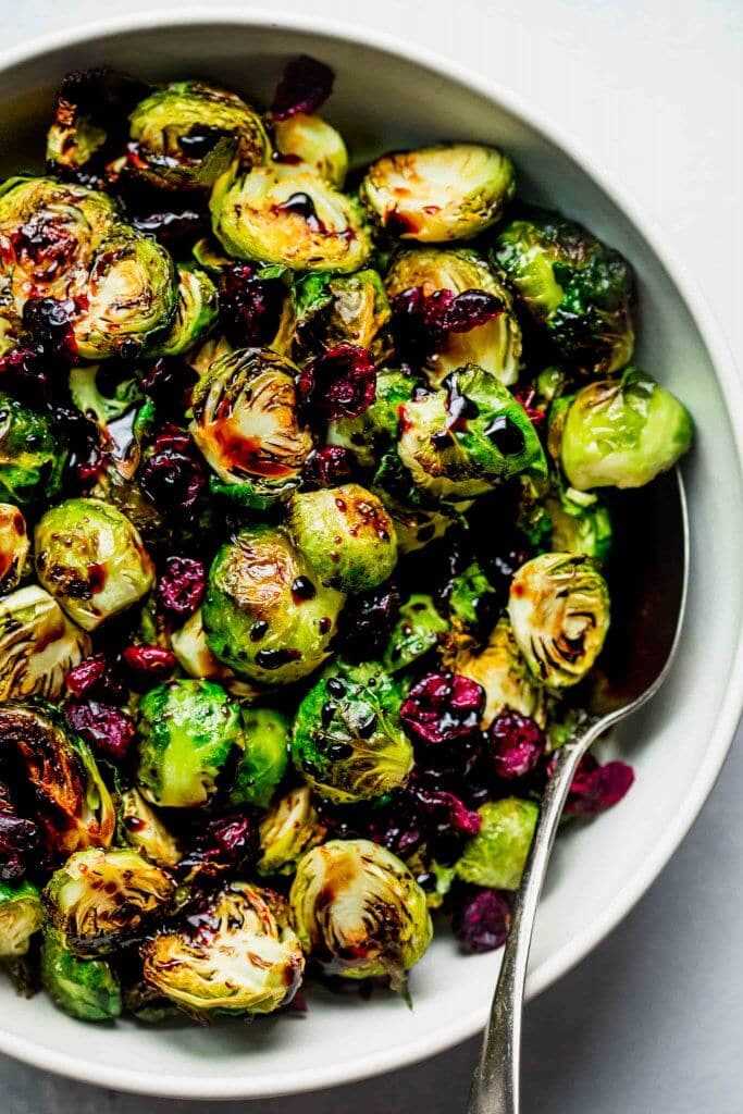 Roasted brussel sprouts in bowl drizzled with balsamic glaze and sprinkled with cranberries.