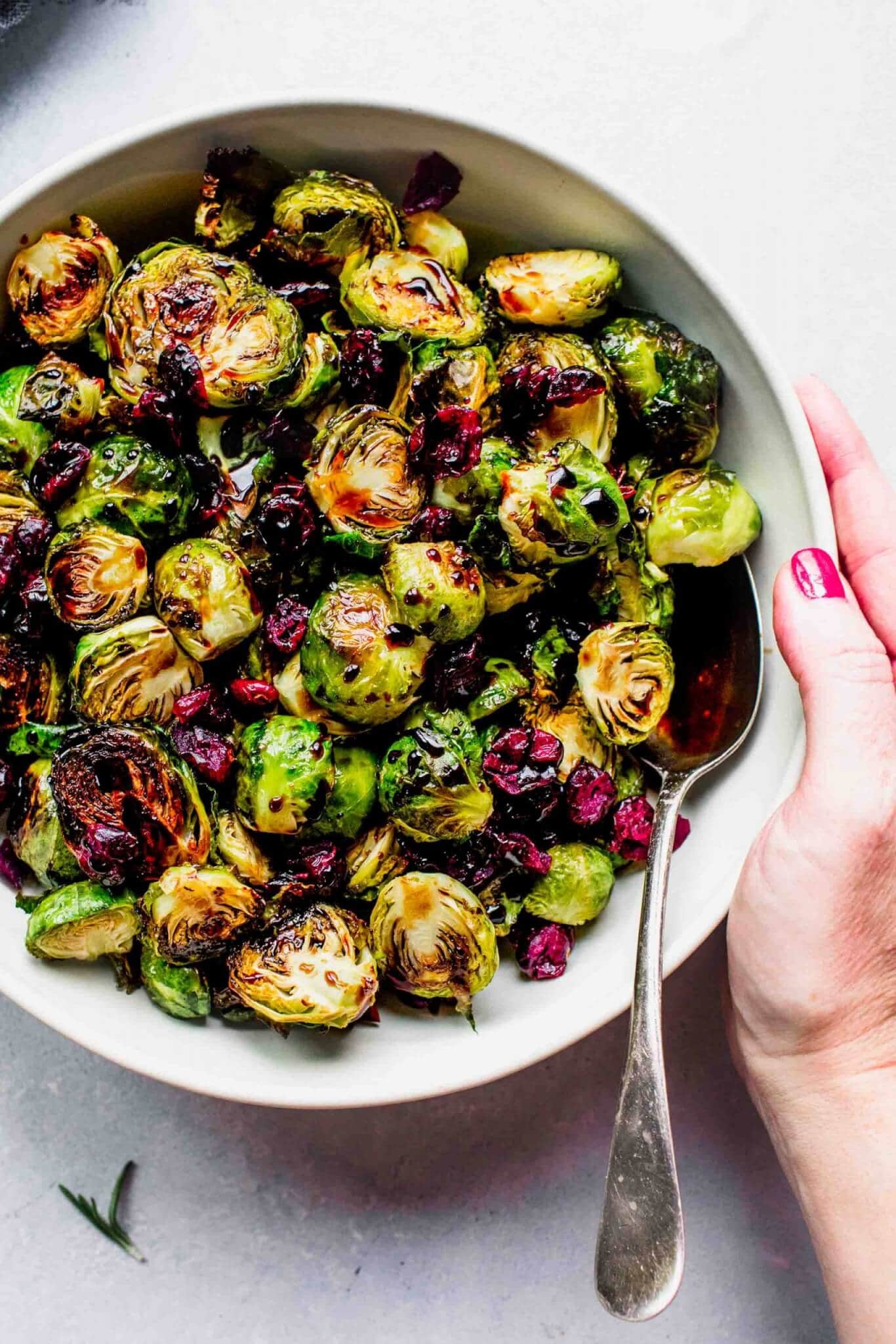 Roasted brussels sprouts in bowl drizzled with balsamic glaze and sprinkled with cranberries.