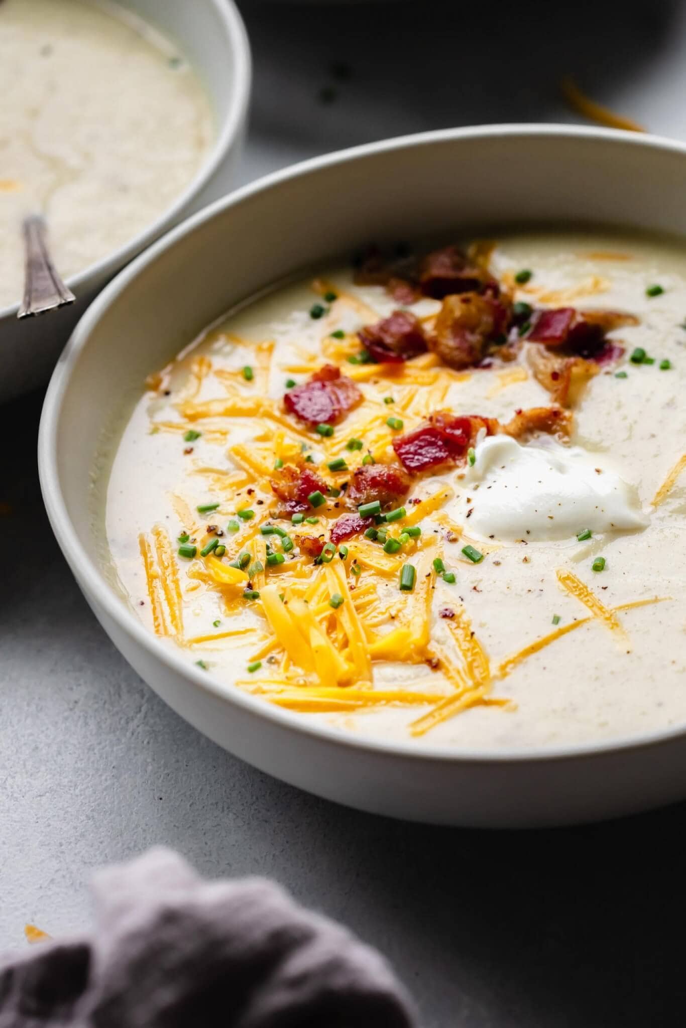 Side view of bowl of cauliflower cheese soup topped with bacon, cheese and sour cream.