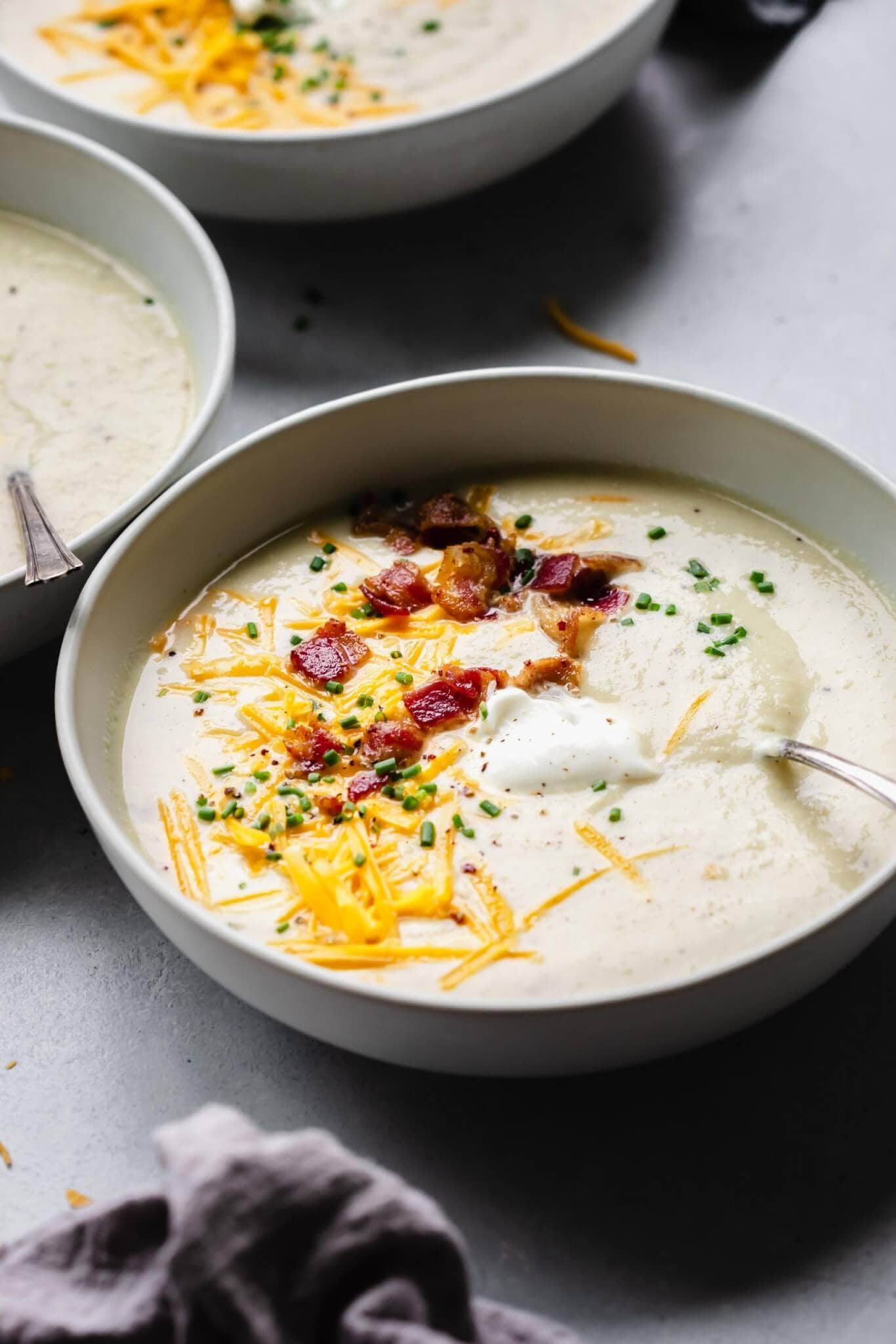 Side view of bowl of cauliflower cheese soup topped with bacon, cheese and sour cream.