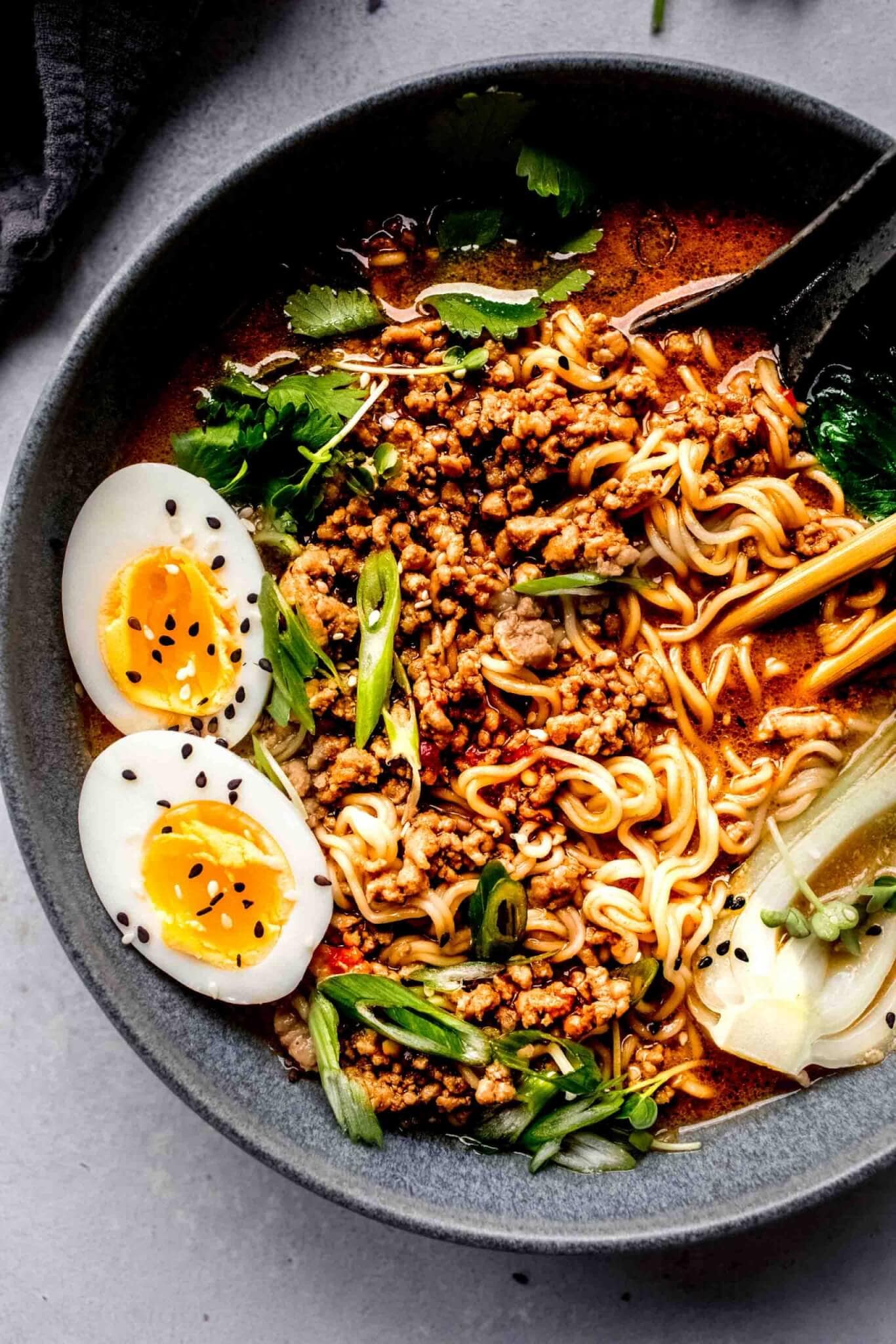 Bowl of dan dan noodles topped with bok choy, green onions and a soft boiled egg.