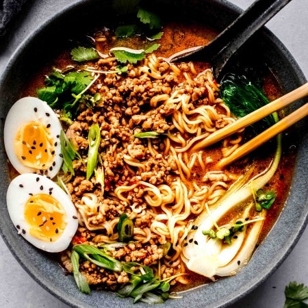 Bowl of dan dan noodles topped with bok choy, green onions and a soft boiled egg.