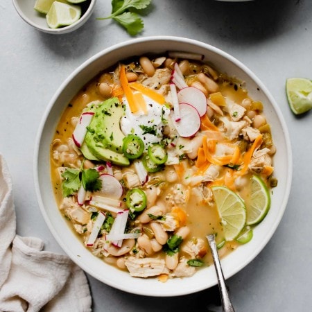 2 bowls of white chicken chili topped with cheese, sour cream and radishes.