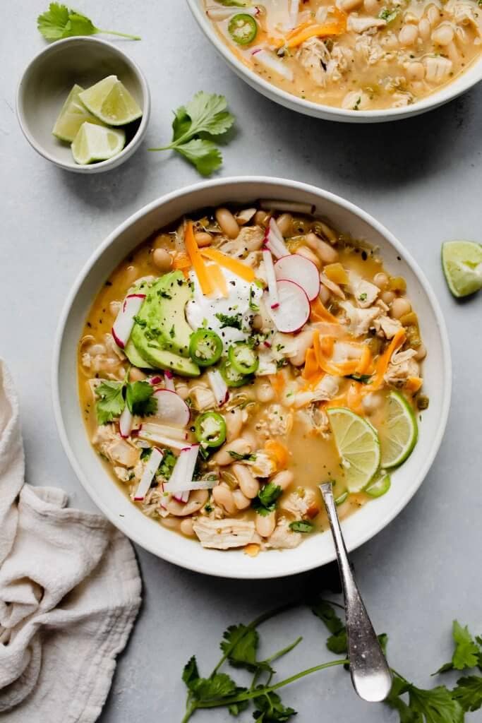 2 bowls of white chicken chili topped with cheese, sour cream and radishes.