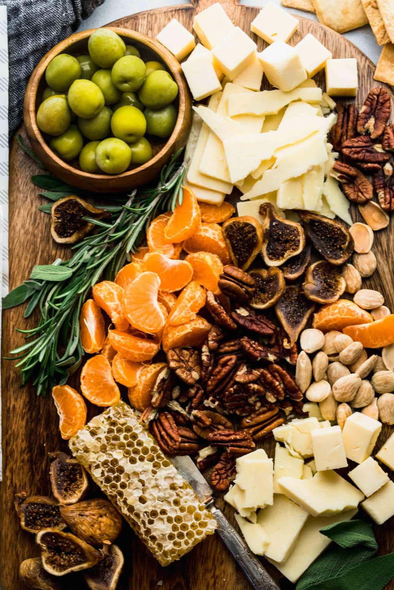 Close up of cheeses, nuts, olives and fruits arranged on wooden serving board.