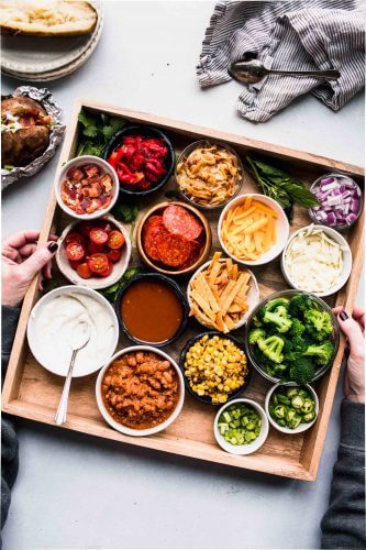 Wooden tray with toppings for baked potatoes on counter.