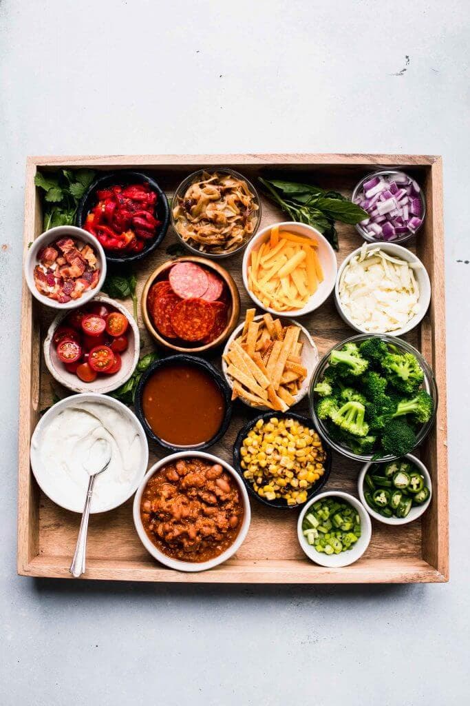 Baked potato toppings on wooden tray.