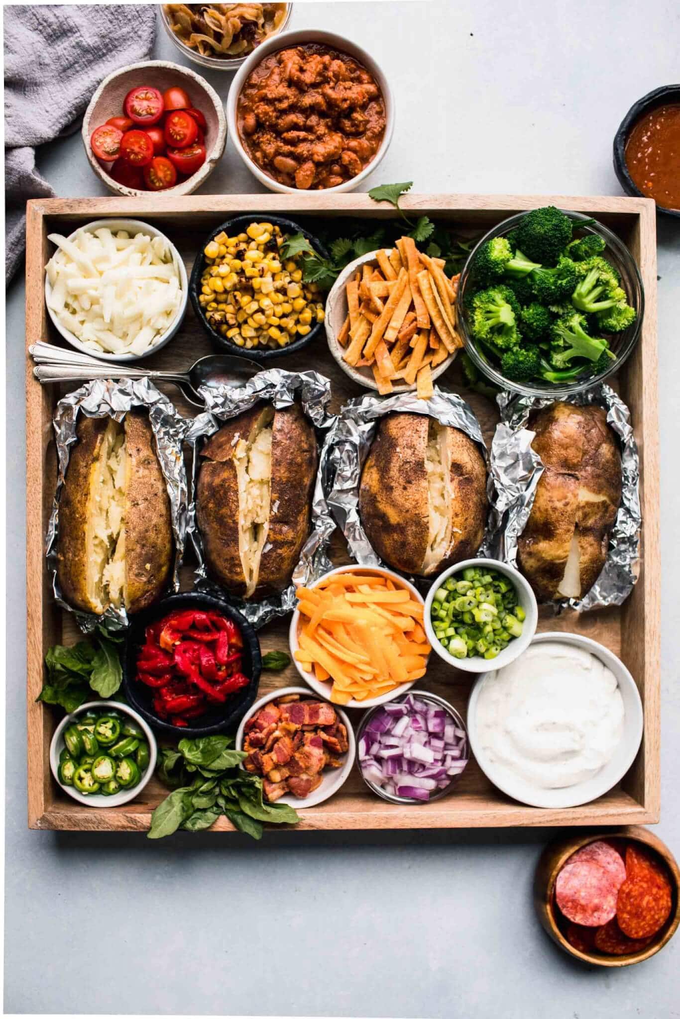 Baked potatoes on wooden tray surround with toppings.