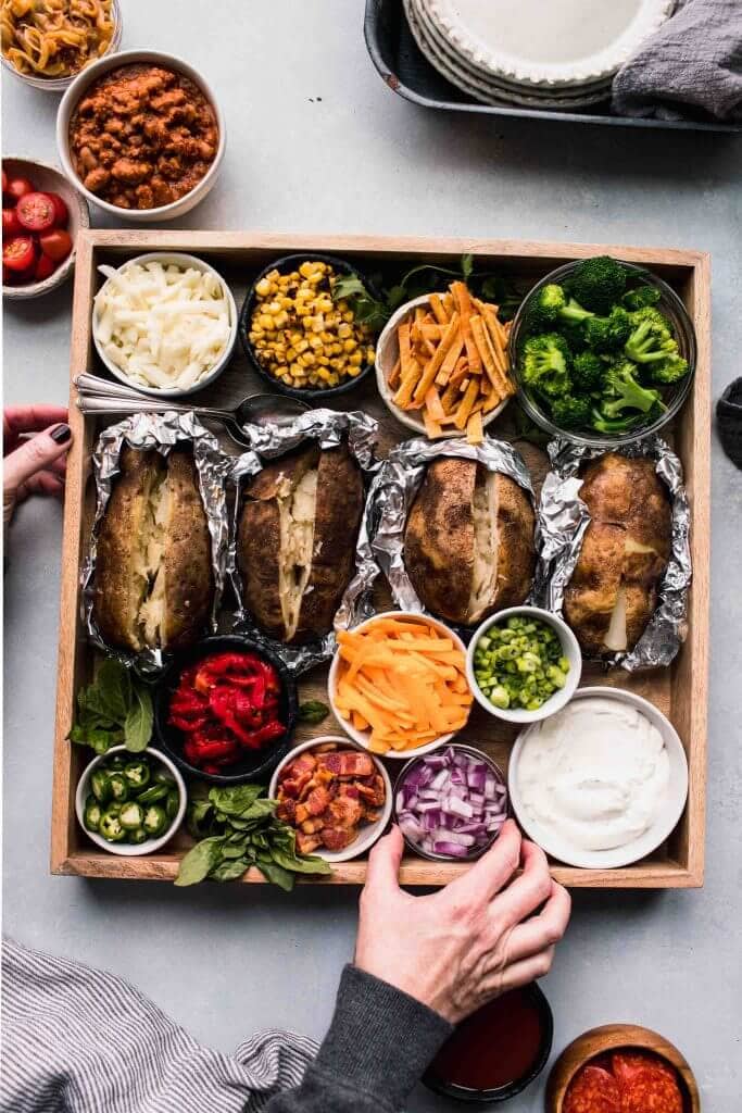 Baked potatoes and topping ideas on wooden tray to serve.