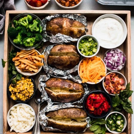 Baked potatoes on wooden tray surround with toppings.
