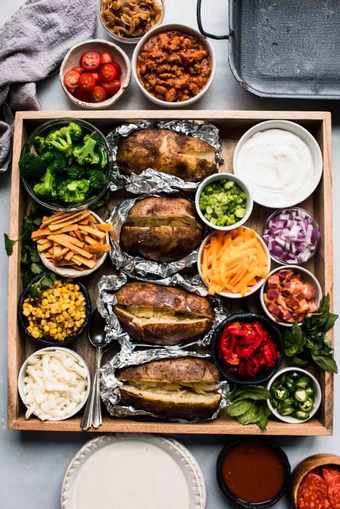 Baked potatoes on wooden tray surround with toppings.