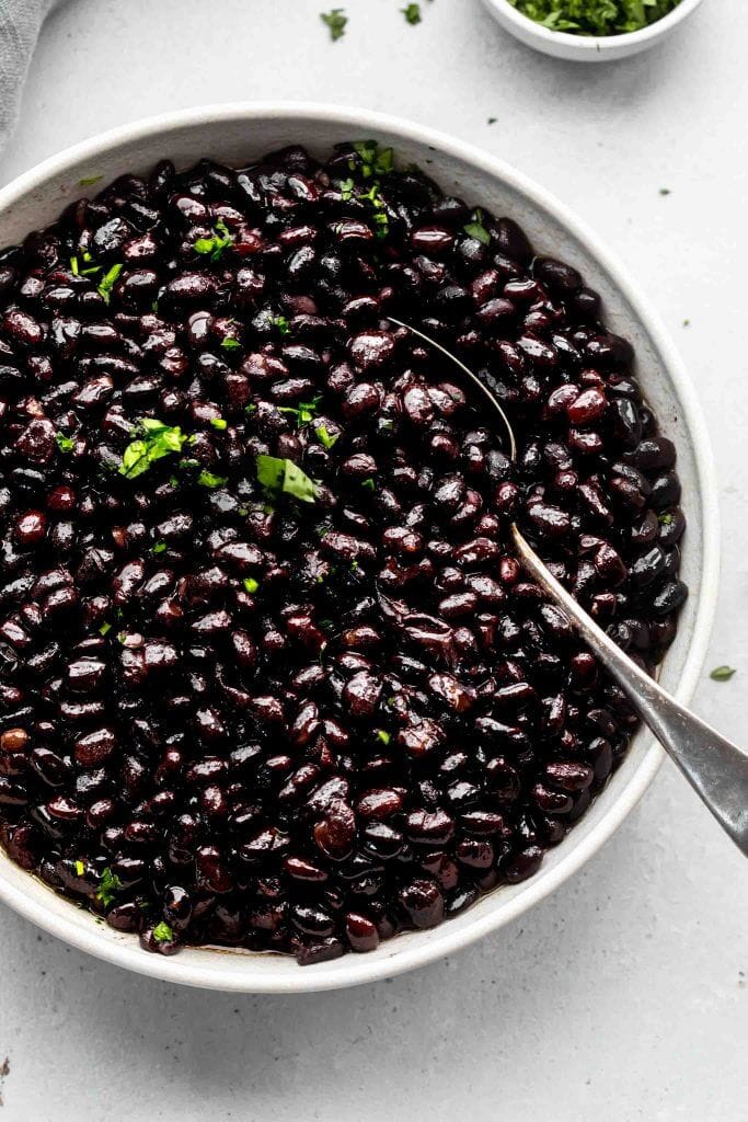 Top shot of black beans in large white bowl with spoon