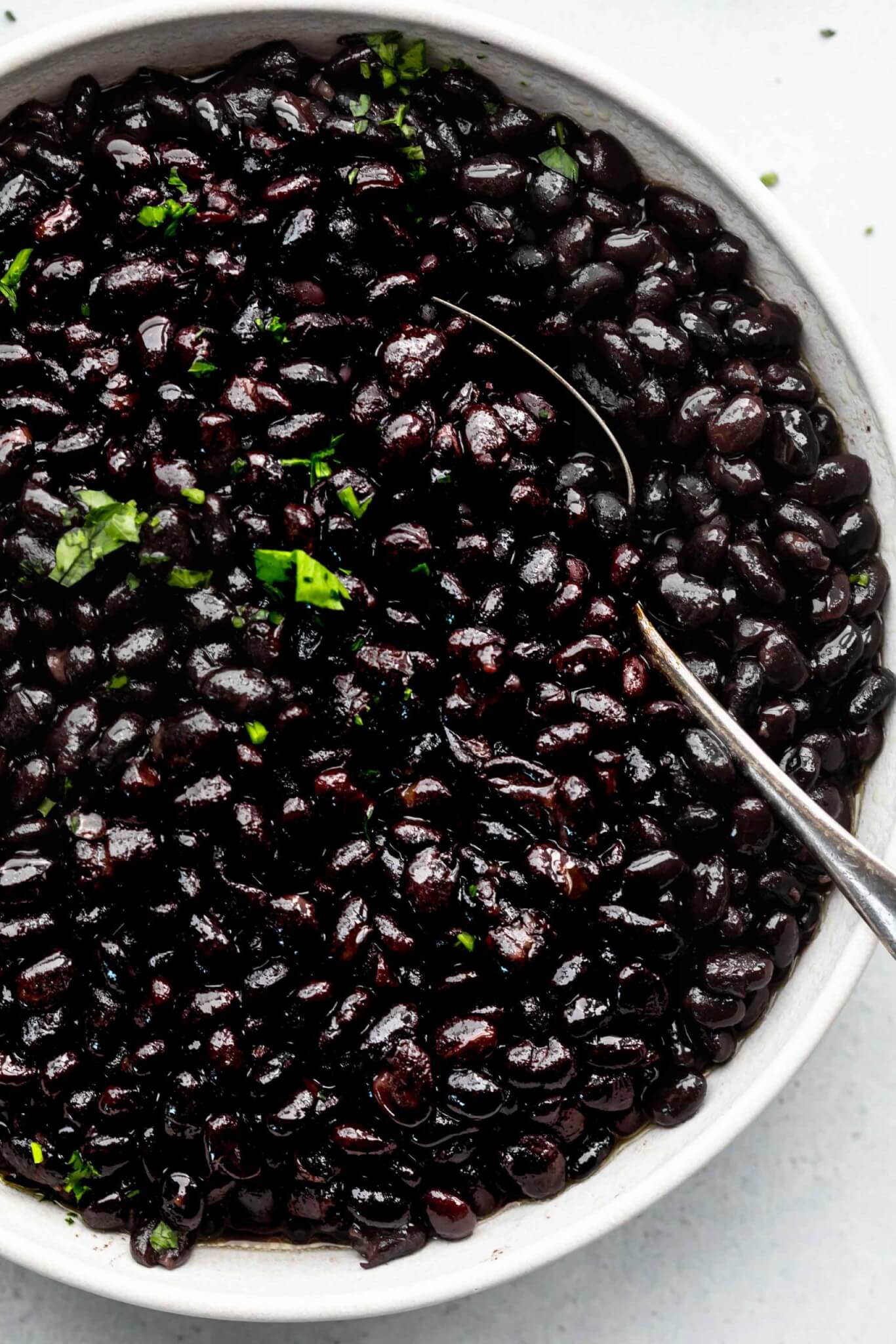 Top shot of black beans in large white bowl with spoon