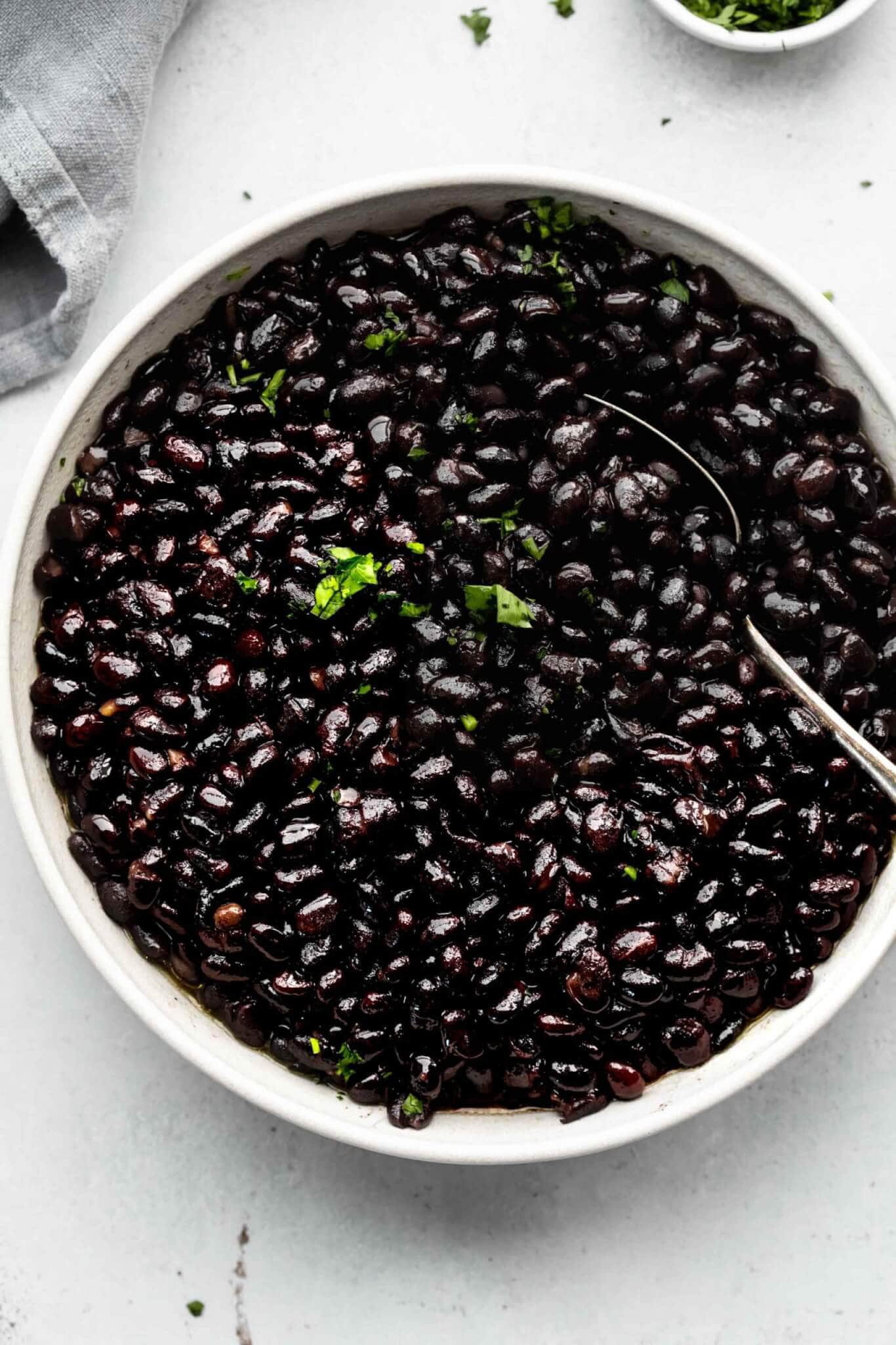 Top shot of black beans in large white bowl with spoon