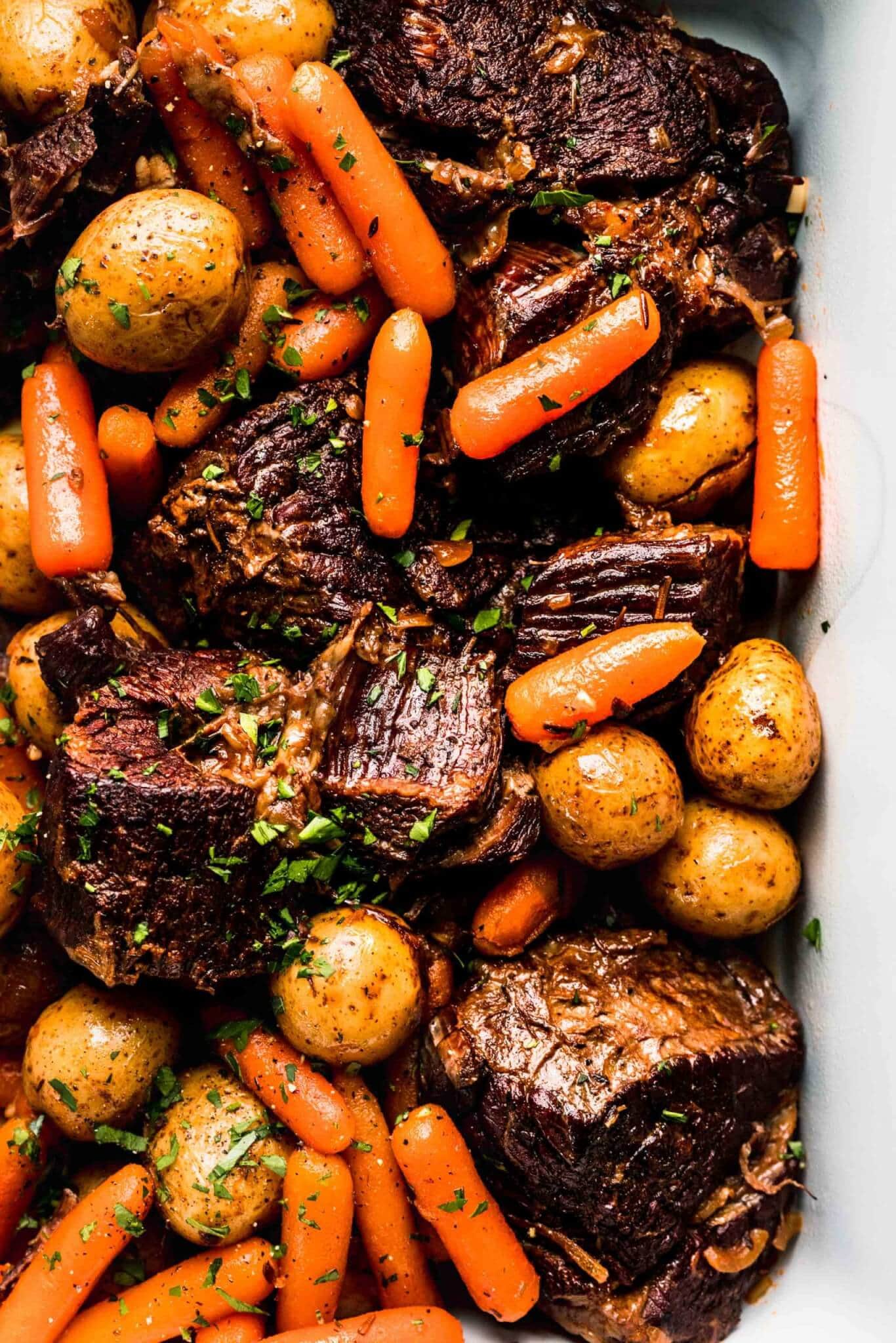 Close view of pot roast, potatoes, and carrots in white serving dish