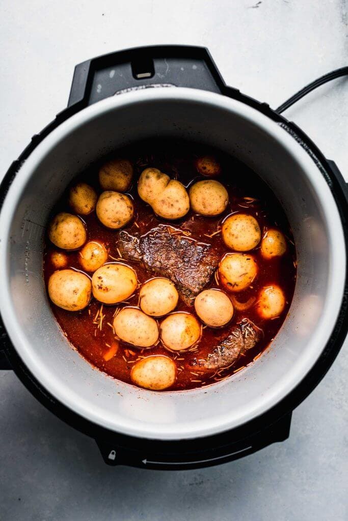 Raw potatoes added on top of roast in pot. 