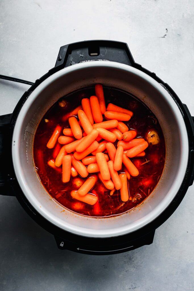 Raw baby carrots added to pot on top of meat and potatoes