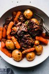Pot roast, potatoes and carrots arranged in white bowl.
