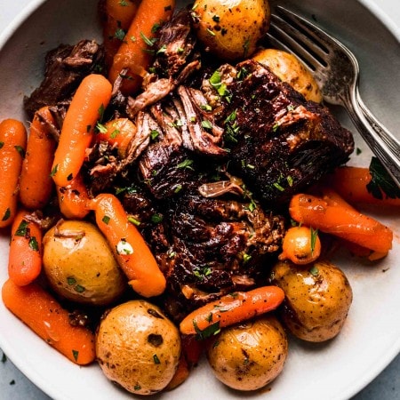 Pot roast, potatoes and carrots arranged in white bowl.
