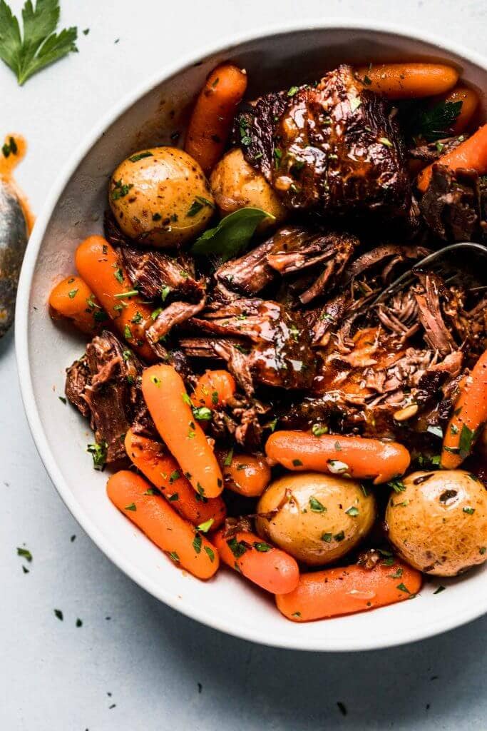 Pot roast, potatoes, and carrots in white bowl.