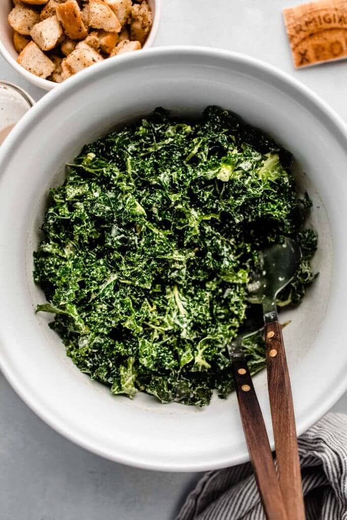 Kale caesar tossed with dressing in large serving bowl.