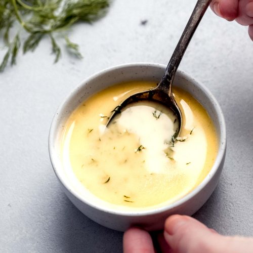 Spoon stirring yellow herb sauce in small white bowl