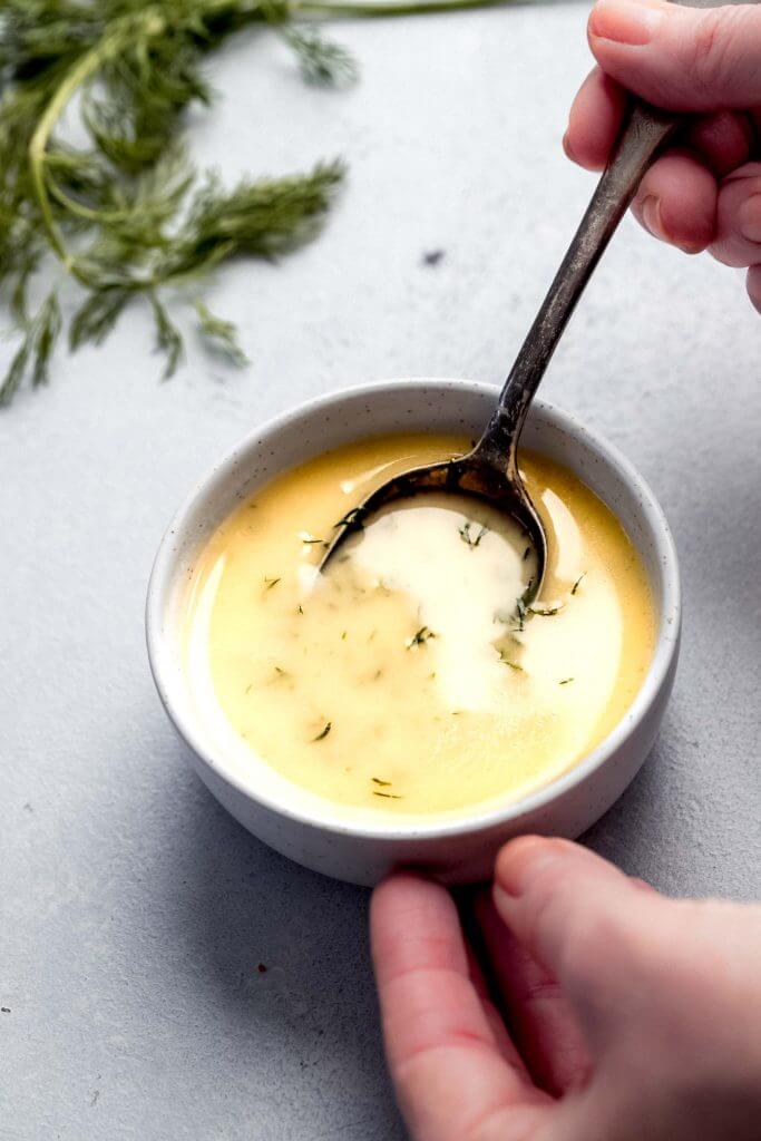 Spoon stirring yellow herb sauce in small white bowl