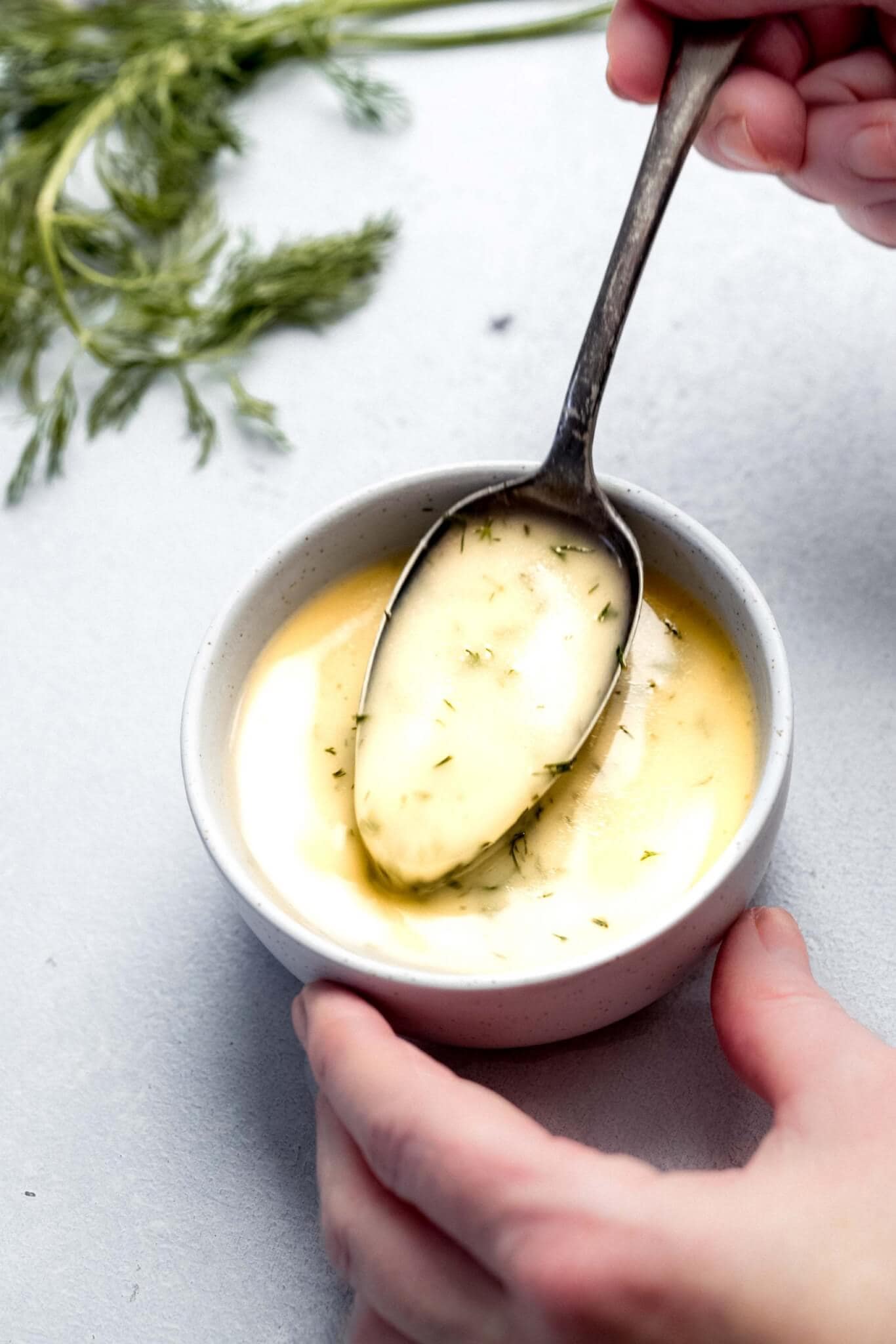 Spoon stirring yellow herb sauce in small white bowl