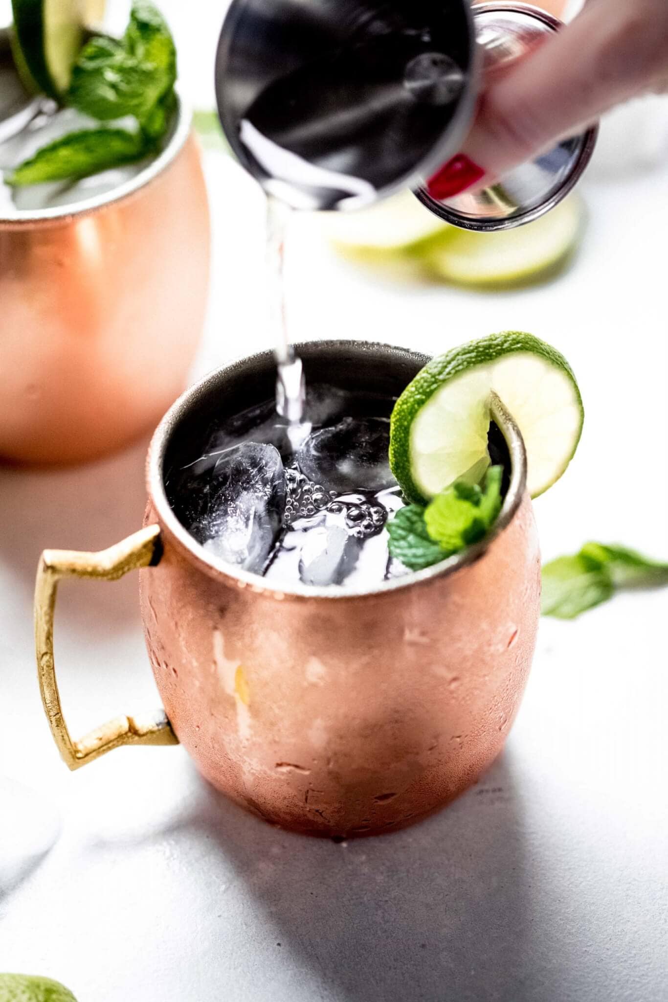 Pouring vodka into copper mug with lime garnish