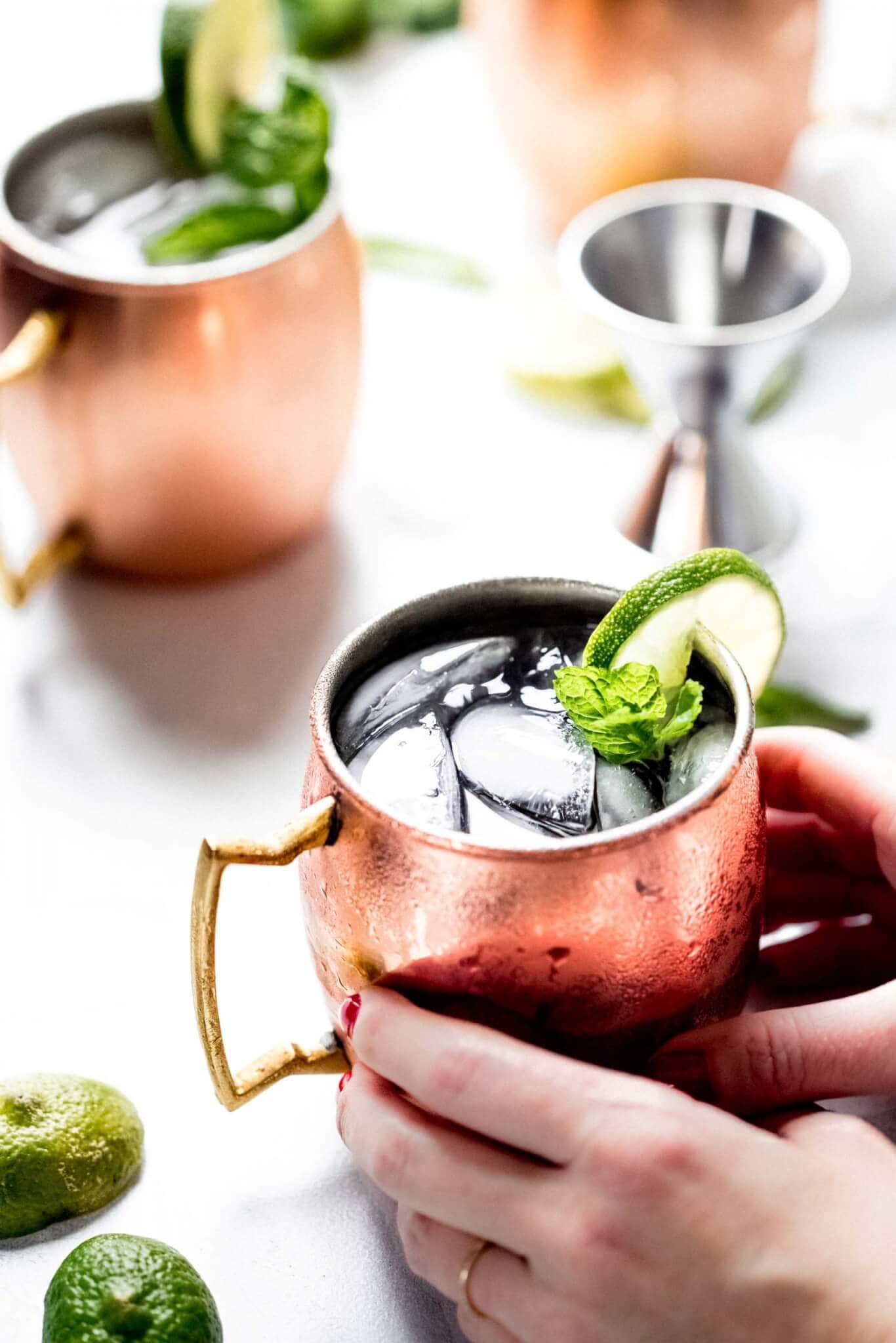 Hands holding moscow mule in copper mug with mug in background