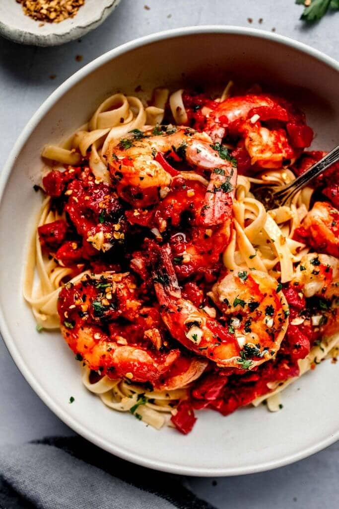 Bowl of shrimp fra diavolo next to bowl of pepper flakes. 