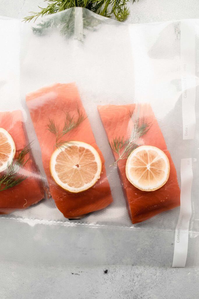 raw salmon with lime wedge and fresh herbs in plastic bag