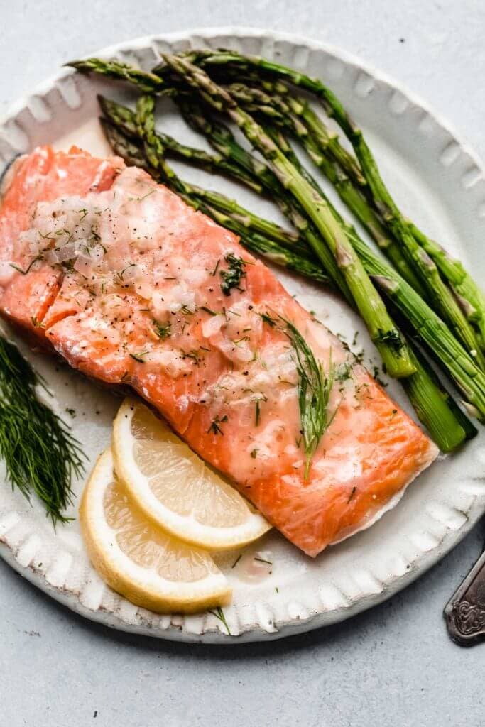 Cooked sous vide salmon with asparagus and lime wedges on white plate