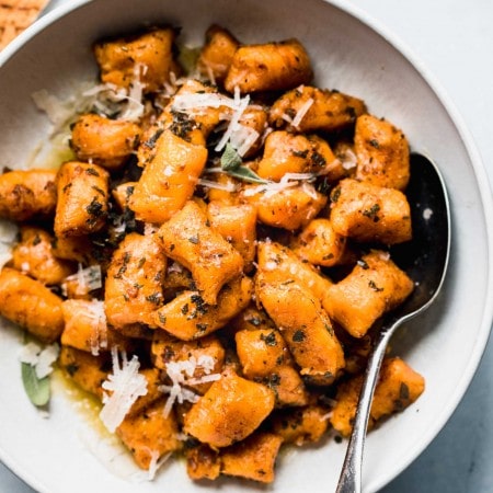 Sweet potato gnocchi in white bowl next to sage leaves and parmesan rind.